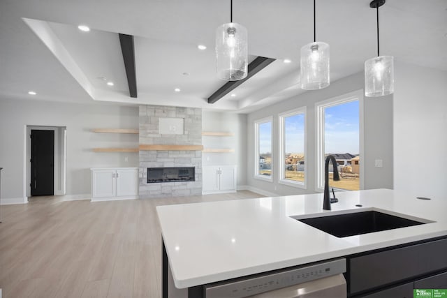 kitchen featuring a fireplace, dishwasher, sink, hanging light fixtures, and light wood-type flooring