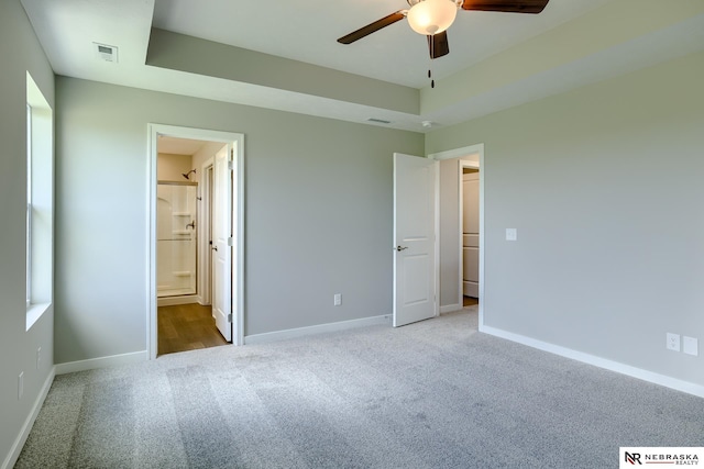 unfurnished bedroom featuring ensuite bathroom, light carpet, and a tray ceiling