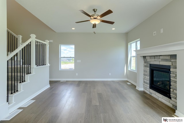 unfurnished living room with a fireplace, plenty of natural light, wood-type flooring, and ceiling fan