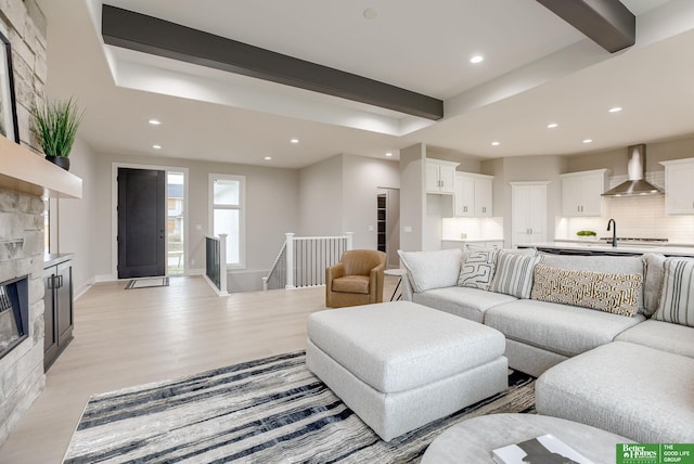 living room featuring beamed ceiling, a fireplace, and light wood-type flooring