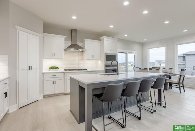 kitchen featuring white cabinets, sink, a kitchen island with sink, and wall chimney range hood