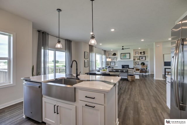 kitchen featuring appliances with stainless steel finishes, decorative light fixtures, white cabinetry, sink, and a center island with sink