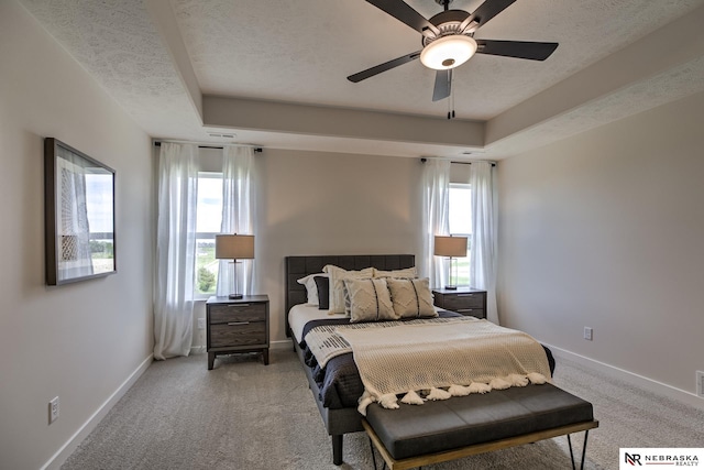 carpeted bedroom featuring ceiling fan, a tray ceiling, and a textured ceiling