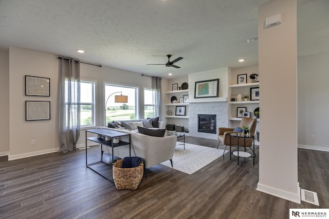 living room featuring a textured ceiling, a large fireplace, dark hardwood / wood-style floors, built in features, and ceiling fan