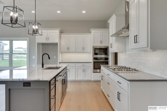 kitchen with sink, white cabinetry, stainless steel appliances, light stone countertops, and an island with sink