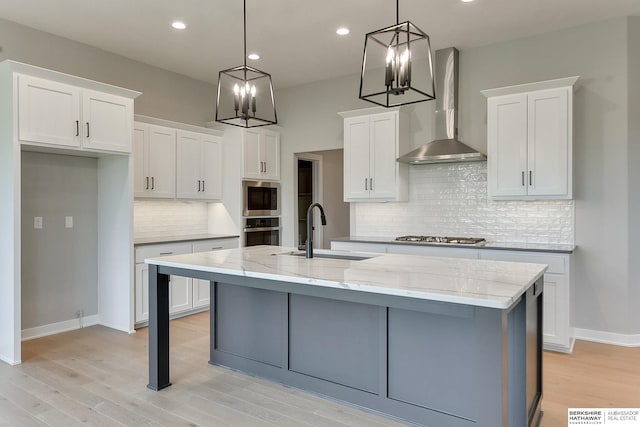 kitchen featuring wall chimney range hood, hanging light fixtures, sink, and white cabinets