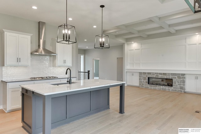 kitchen featuring decorative light fixtures, an island with sink, white cabinets, light stone countertops, and wall chimney exhaust hood