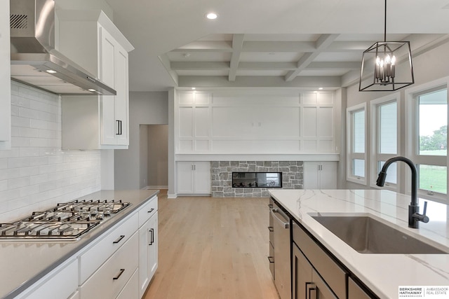 kitchen with wall chimney range hood, sink, appliances with stainless steel finishes, coffered ceiling, and white cabinets