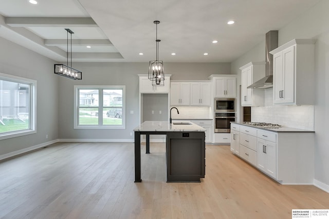 kitchen with hanging light fixtures, wall chimney range hood, appliances with stainless steel finishes, and a center island with sink