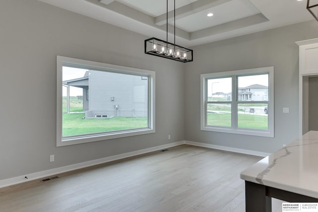 unfurnished dining area with a raised ceiling and light wood-type flooring