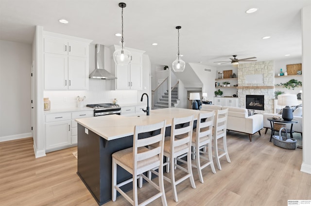 kitchen with decorative light fixtures, white cabinets, wall chimney range hood, gas stove, and a center island with sink