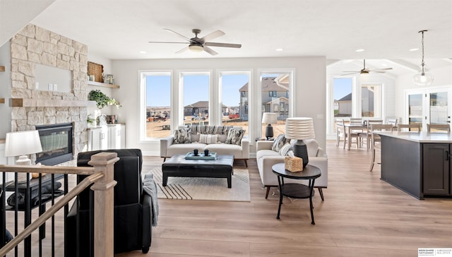 living room featuring ceiling fan, a stone fireplace, and light hardwood / wood-style floors