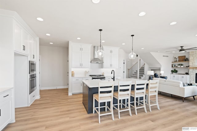 kitchen featuring appliances with stainless steel finishes, wall chimney exhaust hood, a kitchen island with sink, and white cabinets