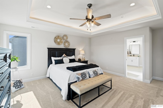 bedroom with a raised ceiling, ensuite bathroom, and light colored carpet