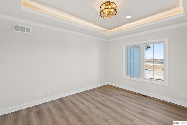 empty room with hardwood / wood-style flooring, crown molding, a raised ceiling, and an inviting chandelier