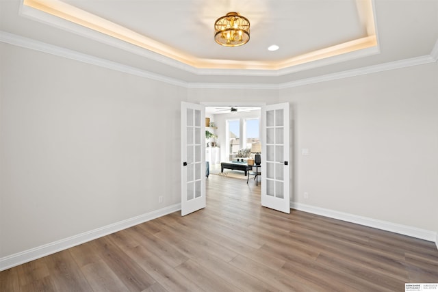 spare room featuring a raised ceiling, wood-type flooring, an inviting chandelier, and french doors