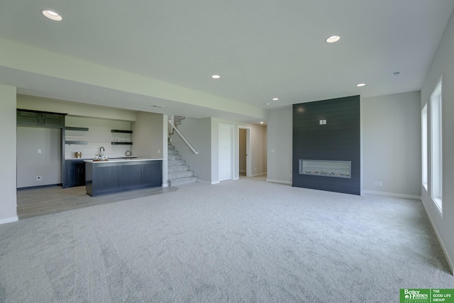 unfurnished living room with light colored carpet, a large fireplace, and indoor wet bar