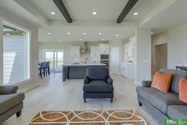 living room with sink, light hardwood / wood-style floors, and beamed ceiling