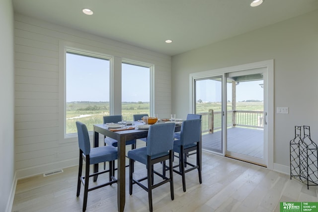 dining room with plenty of natural light, wooden walls, and light hardwood / wood-style flooring