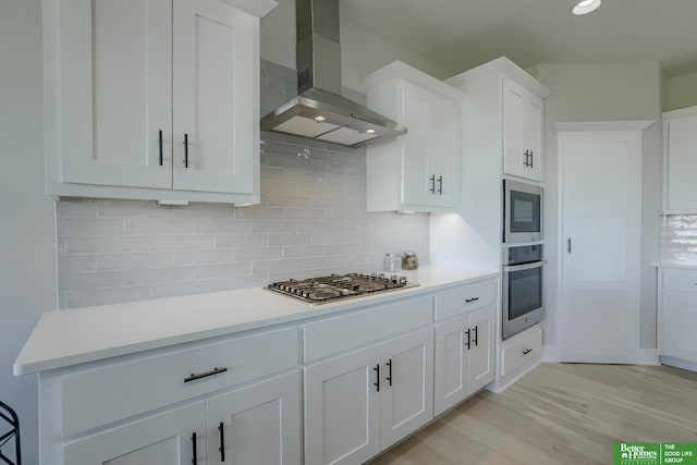 kitchen featuring appliances with stainless steel finishes, white cabinetry, backsplash, range hood, and light wood-type flooring