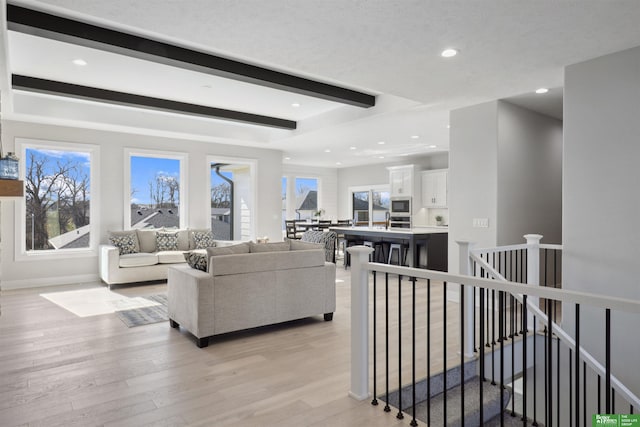 living area with light wood-style floors, baseboards, beamed ceiling, and recessed lighting