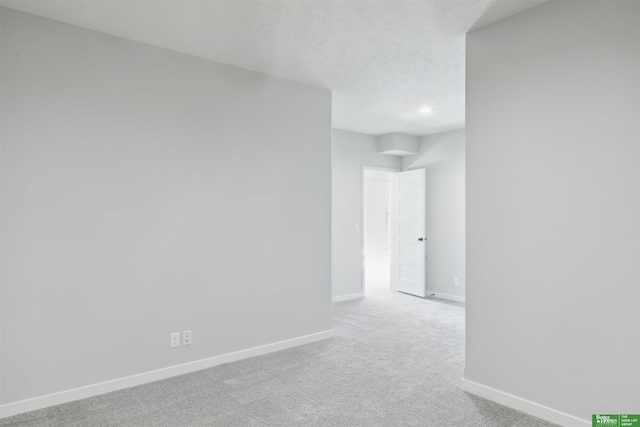 empty room with light colored carpet, a textured ceiling, and baseboards