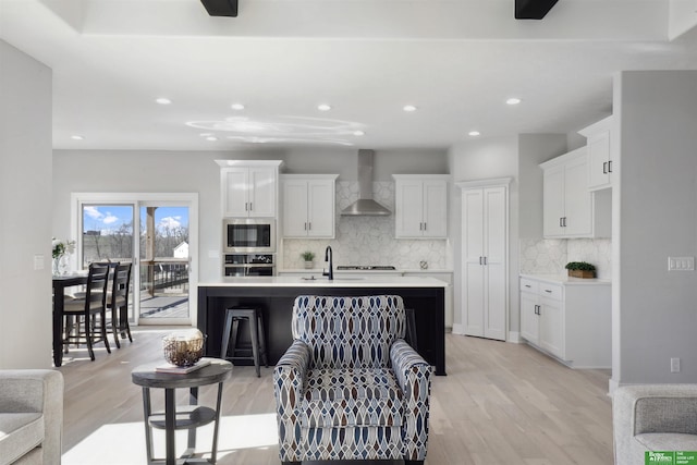 kitchen with appliances with stainless steel finishes, tasteful backsplash, white cabinetry, an island with sink, and wall chimney exhaust hood