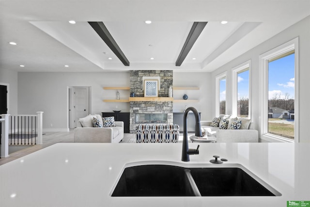 kitchen featuring open floor plan, a sink, light countertops, a stone fireplace, and beam ceiling