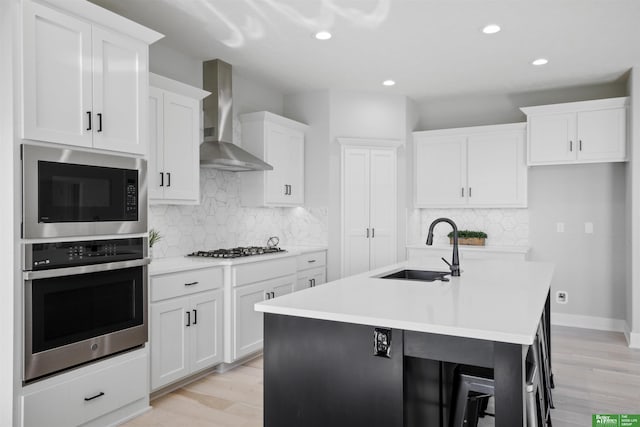 kitchen with appliances with stainless steel finishes, light countertops, a center island with sink, and wall chimney exhaust hood