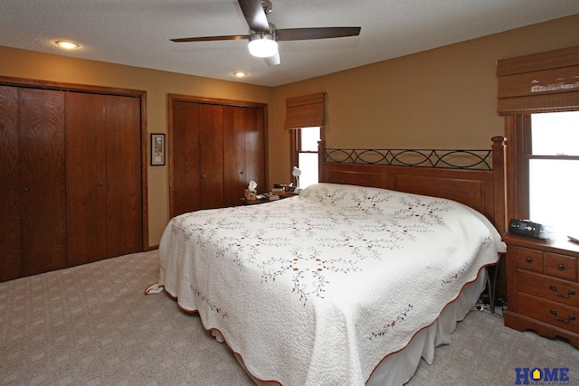 bedroom featuring light carpet, ceiling fan, and multiple closets