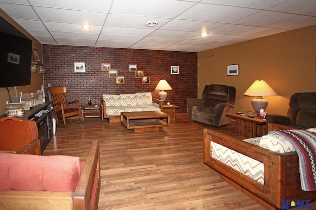 living room featuring a paneled ceiling, visible vents, brick wall, and wood finished floors