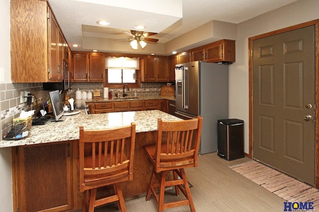 kitchen featuring a tray ceiling, decorative backsplash, high quality fridge, a sink, and a peninsula