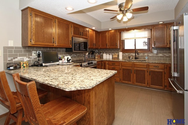 kitchen with stainless steel appliances, brown cabinets, a sink, and a peninsula