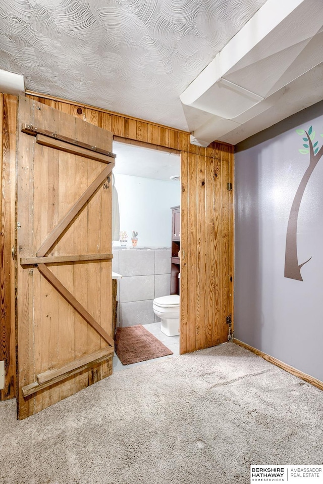 basement featuring a barn door, carpet, and wooden walls