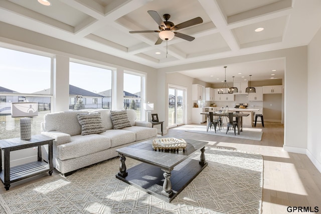 living room with coffered ceiling, ceiling fan with notable chandelier, beam ceiling, and light hardwood / wood-style floors