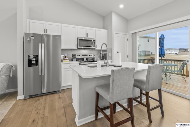 kitchen with appliances with stainless steel finishes, white cabinetry, an island with sink, a breakfast bar area, and backsplash