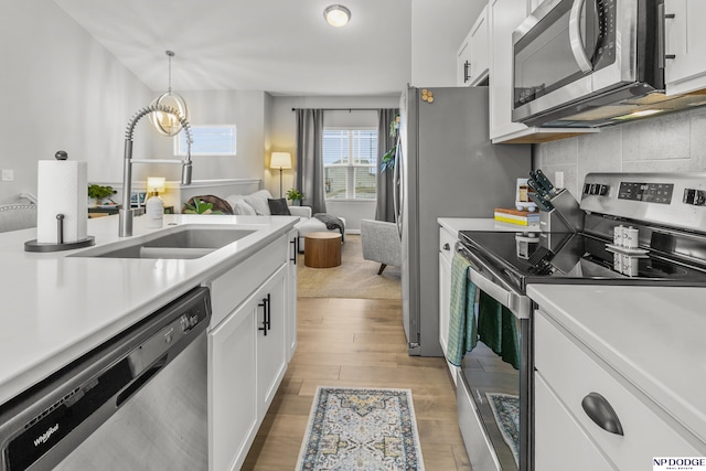 kitchen featuring stainless steel appliances, white cabinetry, sink, and decorative light fixtures