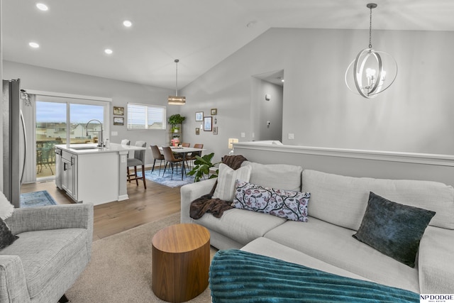 living room with vaulted ceiling, sink, an inviting chandelier, and light hardwood / wood-style flooring