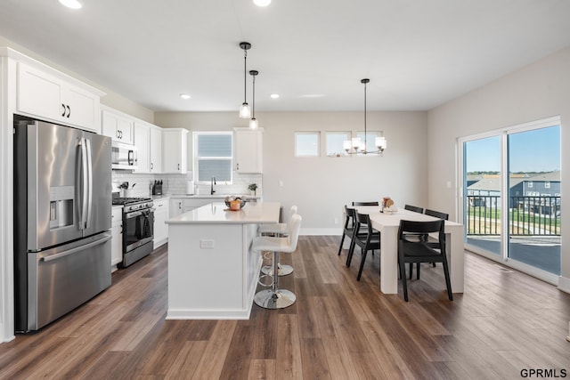 kitchen with a kitchen island, appliances with stainless steel finishes, decorative light fixtures, white cabinets, and backsplash