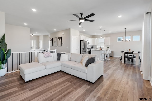 living room featuring ceiling fan with notable chandelier and light wood-type flooring