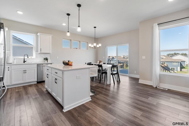 kitchen featuring dark wood-type flooring, white cabinetry, a center island, decorative light fixtures, and stainless steel dishwasher