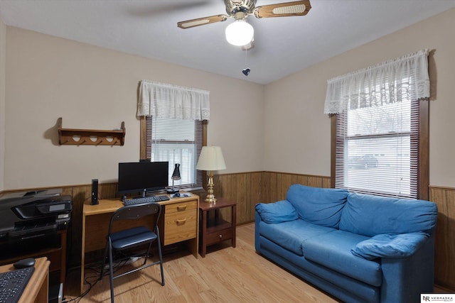 home office featuring ceiling fan, plenty of natural light, wooden walls, and light wood-type flooring