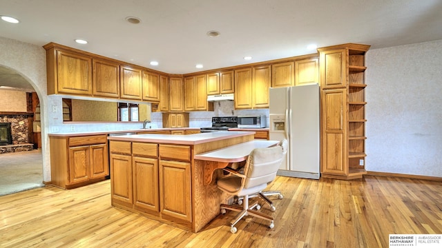 kitchen with white refrigerator with ice dispenser, black range with electric cooktop, a kitchen island, and light wood-type flooring