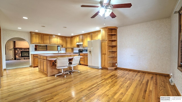 kitchen with a kitchen bar, a center island, light hardwood / wood-style flooring, ceiling fan, and white refrigerator with ice dispenser