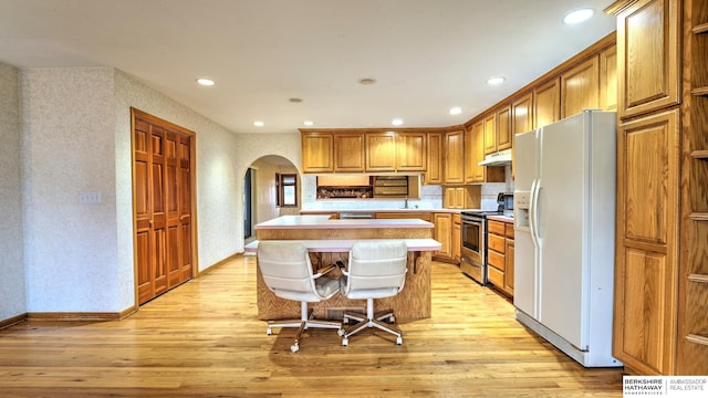 kitchen featuring stainless steel range with electric stovetop, a center island, a kitchen breakfast bar, white refrigerator with ice dispenser, and light hardwood / wood-style floors