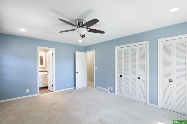 unfurnished bedroom featuring multiple closets, ensuite bathroom, light colored carpet, and ceiling fan