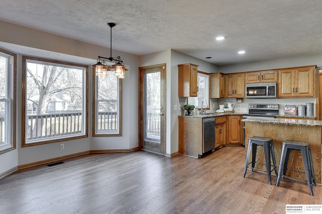 kitchen featuring pendant lighting, appliances with stainless steel finishes, light stone counters, light hardwood / wood-style floors, and a kitchen bar