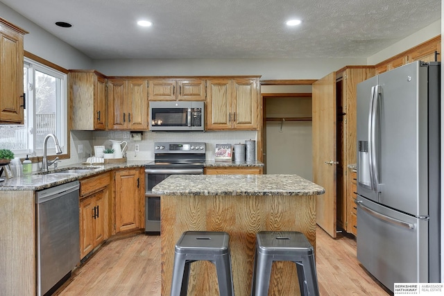 kitchen with sink, a breakfast bar area, light stone counters, a kitchen island, and stainless steel appliances