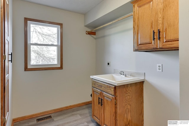 laundry area with cabinets, hookup for an electric dryer, sink, and light wood-type flooring