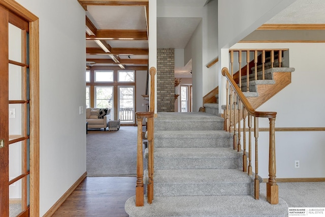 stairs featuring coffered ceiling, beam ceiling, and carpet flooring